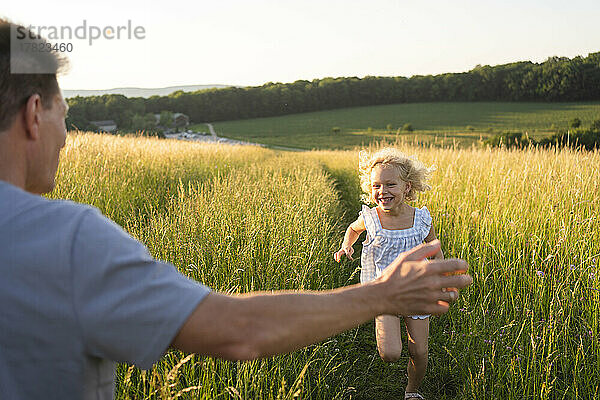 Fröhliches blondes Mädchen rennt auf dem Feld auf den Vater zu