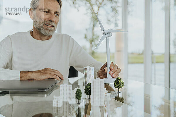 Lächelnder reifer Mann mit Windturbinenmodell am Tisch sitzend