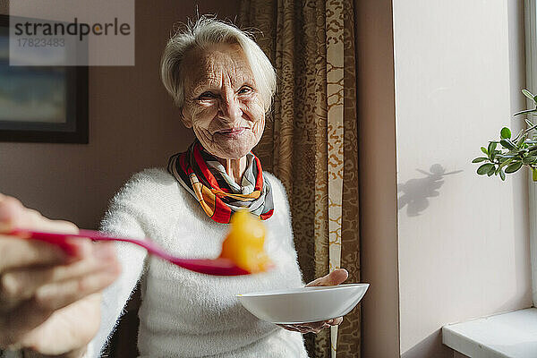 Lächelnde ältere Frau mit kurzen weißen Haaren  die Essen anbietet