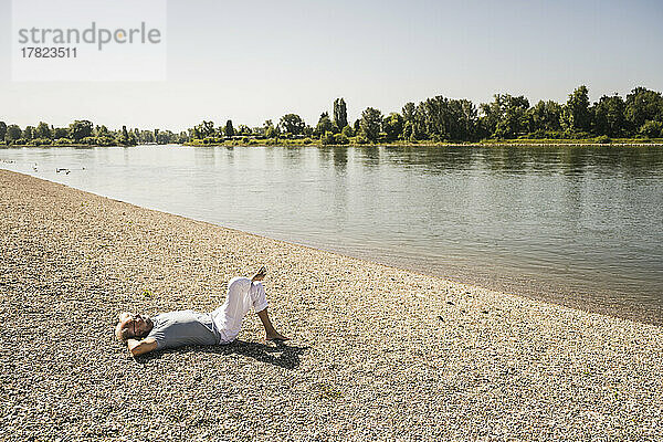 Man with hands behind head resting at riverbank