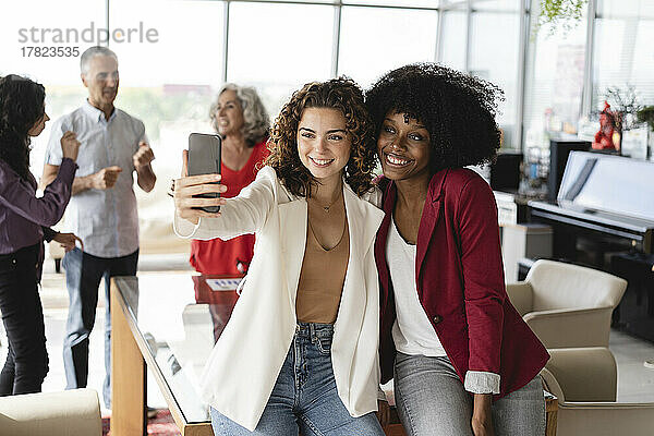 Lächelnde Geschäftskollegen machen im Büro ein Selfie per Smartphone