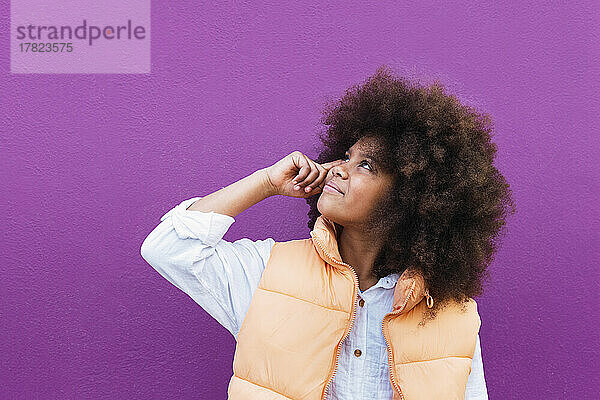 Mädchen mit Afro-Frisur blickt vor violettem Hintergrund nach oben