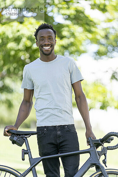 Glücklicher junger Mann mit Fahrrad im Park