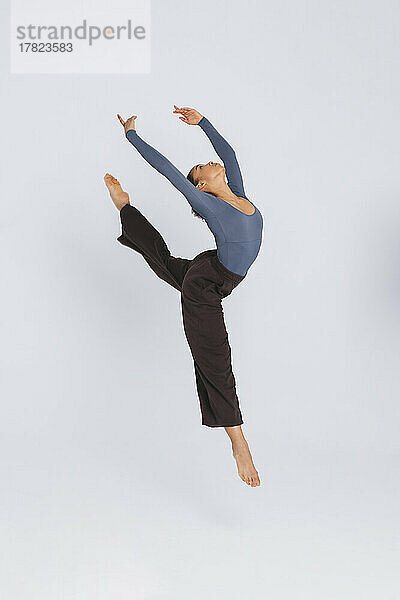 Junge flexible Balletttänzerin mit erhobenen Armen vor weißem Hintergrund