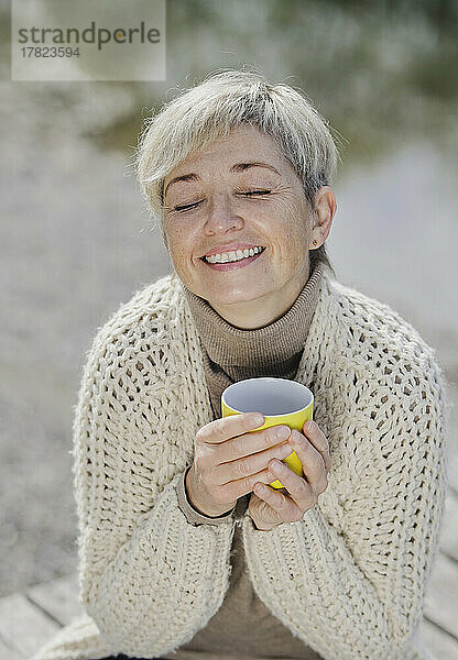 Lächelnde reife Frau mit geschlossenen Augen  die eine Tasse hält