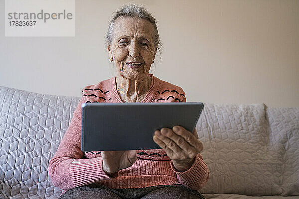 Glückliche ältere Frau benutzt Tablet-PC im Wohnzimmer