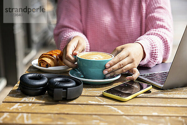 Frau mit Kaffeetasse sitzt im Straßencafé