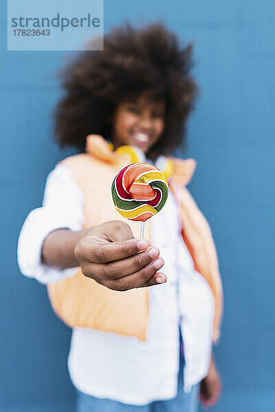 Girl holding colorful candy in front of blue wall