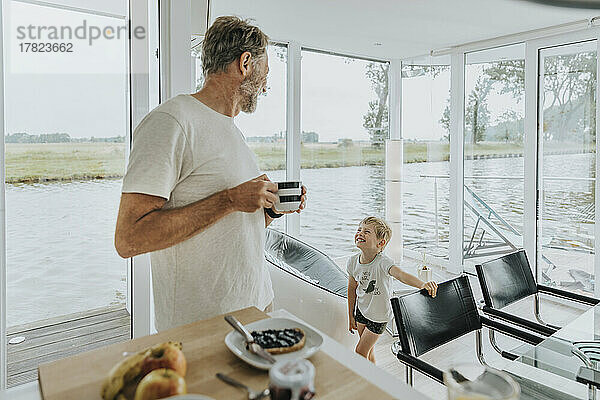 Glücklicher Sohn mit Vater  der zu Hause eine Kaffeetasse hält
