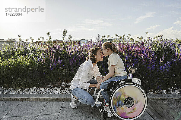 Tochter im Rollstuhl küsst Mutter im Park