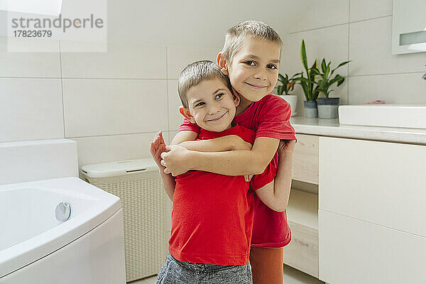 Smiling boy embracing brother from behind in bathroom at home