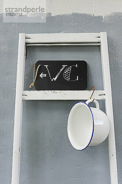 Chamber pot hanging on ladder holding chalkboard restroom sign