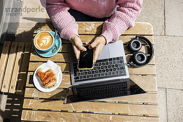 Frau sitzt an einem sonnigen Tag im Straßencafé und benutzt ihr Mobiltelefon