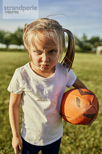 Blondes Mädchen mit Rugbyball macht an einem sonnigen Tag auf dem Sportplatz ein Gesicht