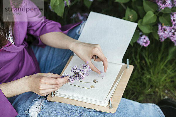 Frau sitzt mit lila Blume und Buch