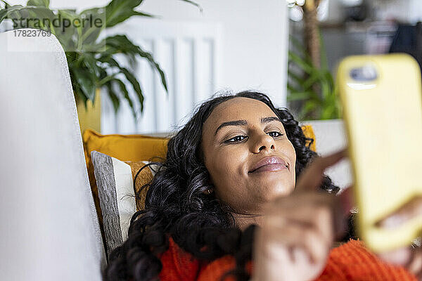 Lächelnde Frau entspannt sich mit Smartphone auf dem Sofa