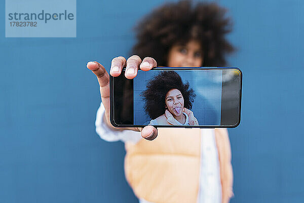 Selfie eines Mädchens  das die Zunge herausstreckt  auf dem Bildschirm des Smartphones zu sehen