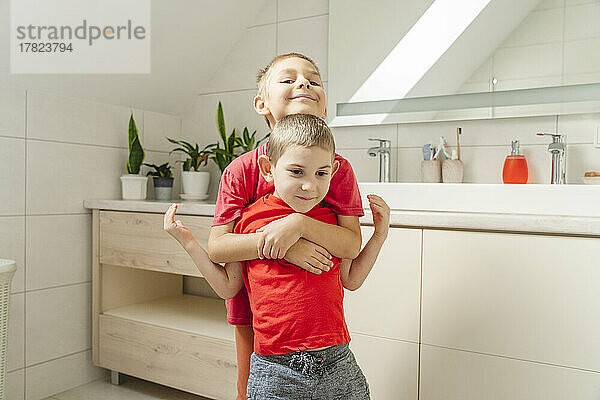 Lächelnder Junge umarmt Bruder von hinten im Badezimmer