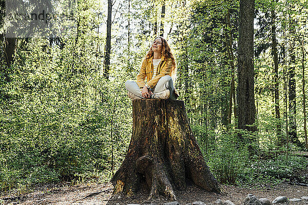Frau sitzt mit gekreuzten Beinen auf Baumstumpf im Wald