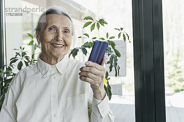 Glückliche ältere Frau mit Smartphone steht im Café