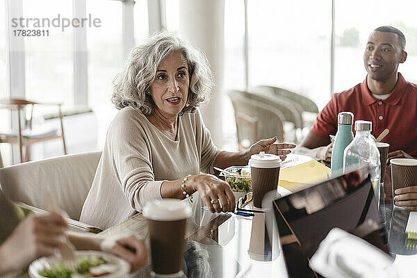 Ältere Geschäftsfrau sitzt mit Geschäftsmann und diskutiert am Tisch im Büro