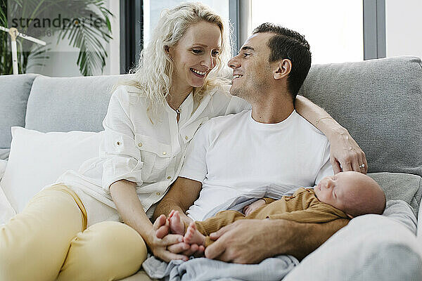 Mann mit Baby im Arm sitzt neben Frau auf Sofa zu Hause