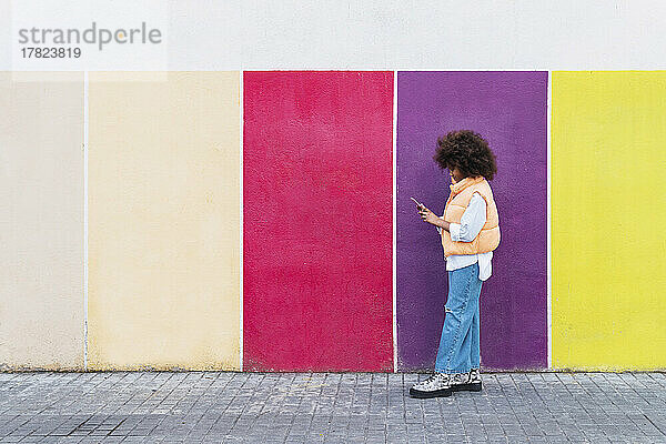 Mädchen benutzt Smartphone an bunter Wand