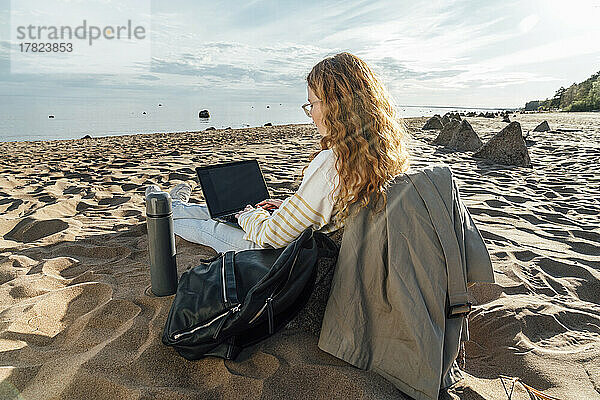 Junge Frau benutzt Laptop am Strand an einem sonnigen Tag