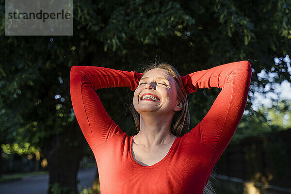 Fröhliche Frau mit den Händen hinter dem Kopf  die das Sonnenlicht genießt