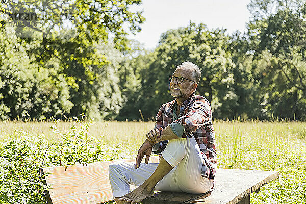 Lächelnder älterer Mann mit Brille sitzt auf Picknicktisch