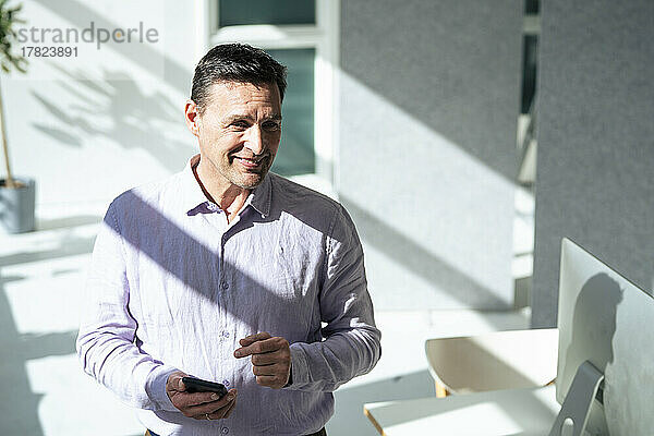 Lächelnder Geschäftsmann hält Smartphone im Büro