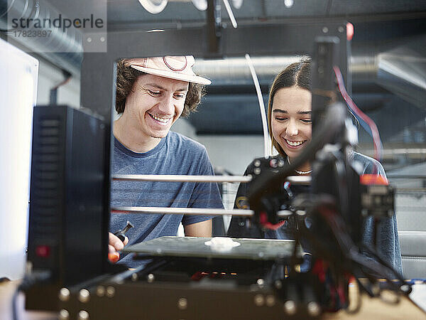 Lächelnde Ingenieure arbeiten in der Werkstatt mit 3D-Drucker