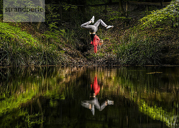 Junge Frau macht Handstand am See im Wald