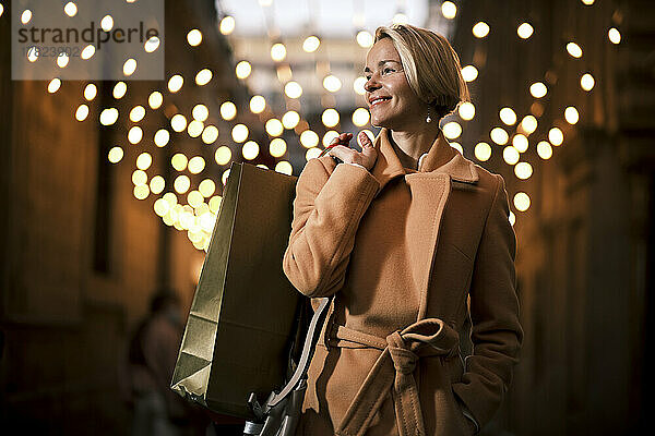 Glückliche Frau hält nachts Einkaufstasche