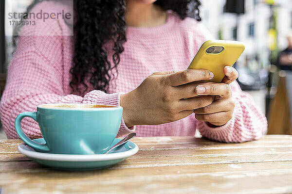 Junge Frau  die SMS über ihr Mobiltelefon sendet und mit einer Kaffeetasse im Straßencafé sitzt