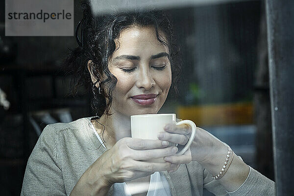 Schöne Frau mit geschlossenen Augen  die durch ein Glasfenster Kaffee riecht