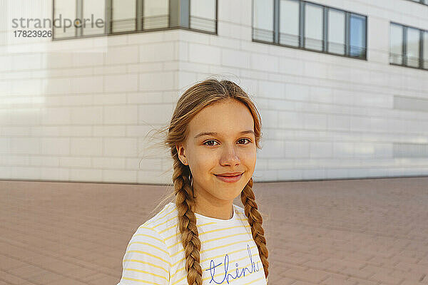 Lächelndes Mädchen mit geflochtenen Haaren  das vor dem Gebäude steht