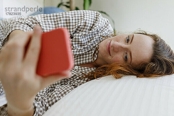 Frau benutzt Smartphone und liegt zu Hause im Bett
