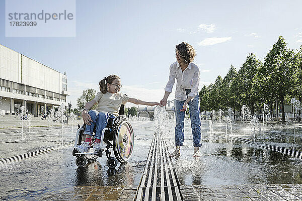 Mädchen im Rollstuhl spielt mit Mutter am Brunnen im Park