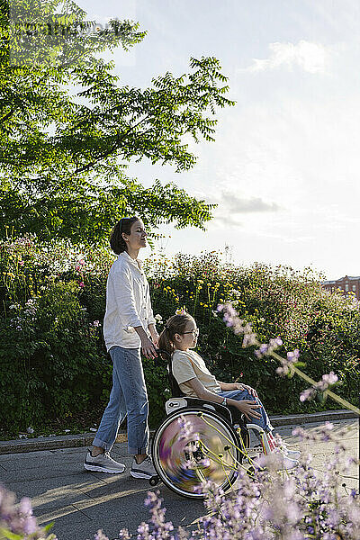 Frau schiebt Tochter mit Behinderung  die im Rollstuhl im Park sitzt