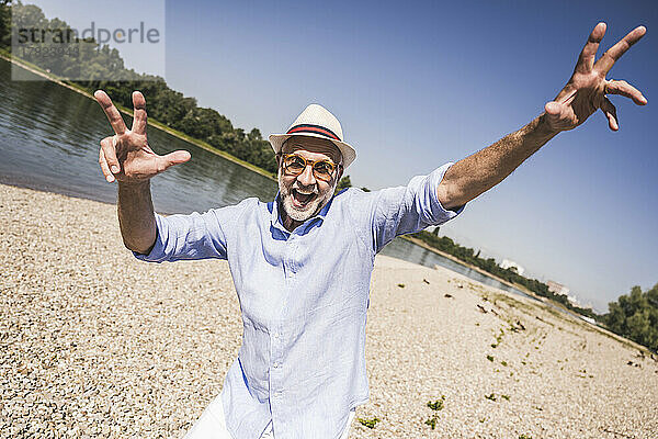 Verspielter älterer Mann am Flussufer an sonnigem Tag