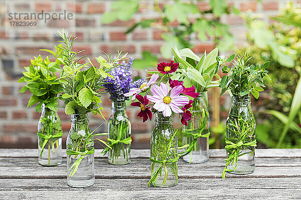 Frische Kräuter und Blumen in dekorierten Glasflaschen stehen auf einem Balkontisch