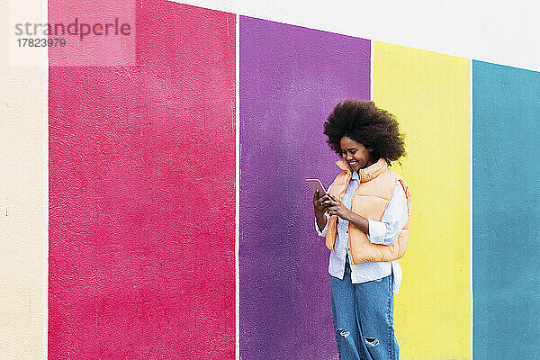Happy girl using smart phone by colorful wall