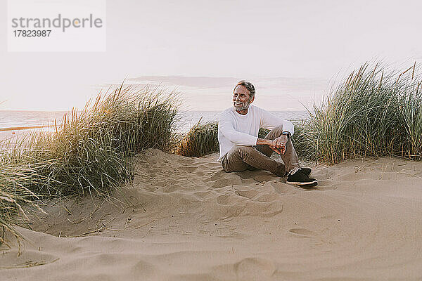 Glücklicher Mann sitzt auf Sanddüne am Strand