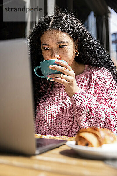 Junge Frau trinkt Kaffee mit Laptop im Straßencafé