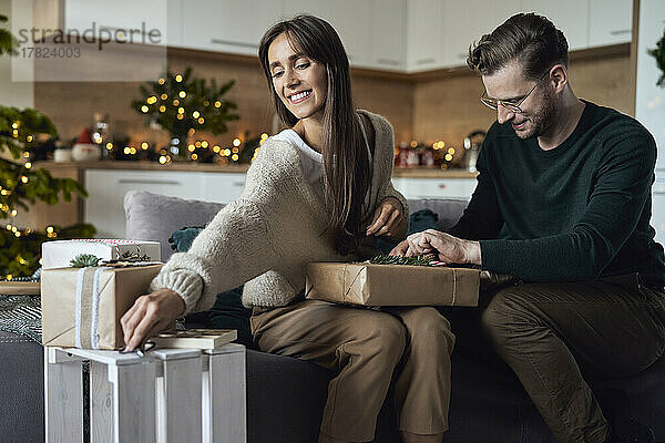 Mann verpackt Geschenkbox von Frau im Wohnzimmer zu Weihnachten