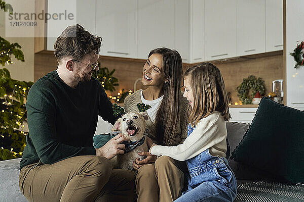 Lächelnde Familie mit Hund  die gemeinsam die Weihnachtszeit zu Hause genießt
