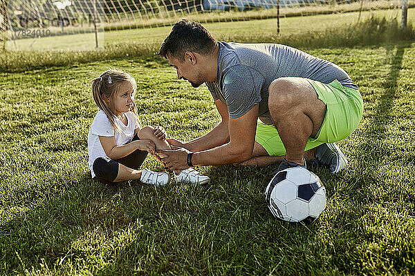 Vater tröstet verletzte Tochter  die auf Sportplatz sitzt