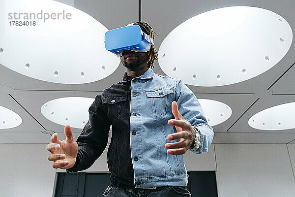 Mann gestikuliert mit Virtual-Reality-Headset unter beleuchteter Decke