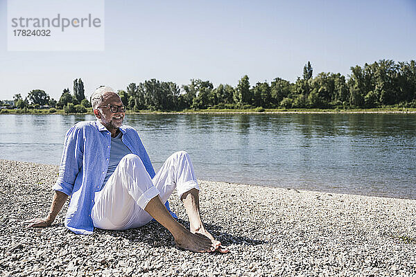 Lächelnder älterer Mann sitzt am Flussufer